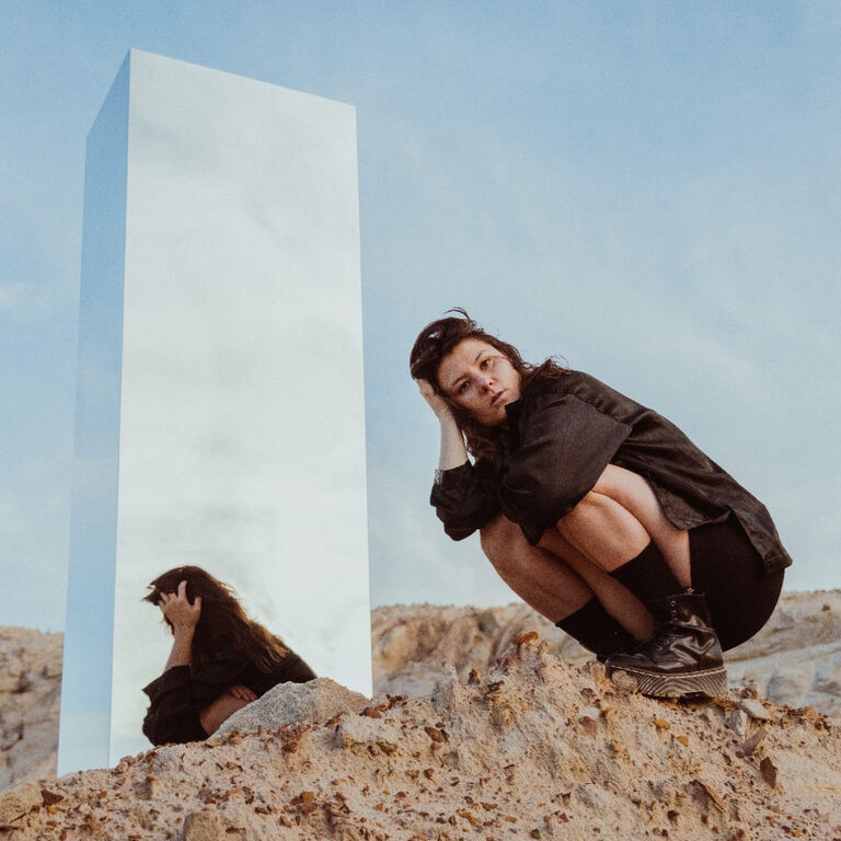 Kate Dillon on sand with a reflective pillar