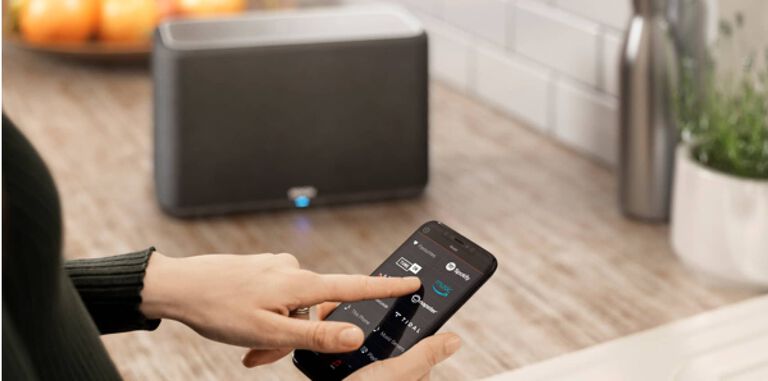 A woman controlling her Denon Home through the HEOS app