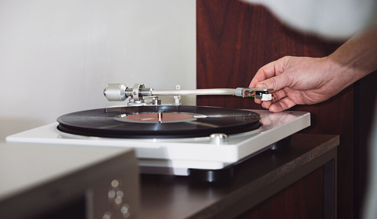 A person lowering the arm of the record player